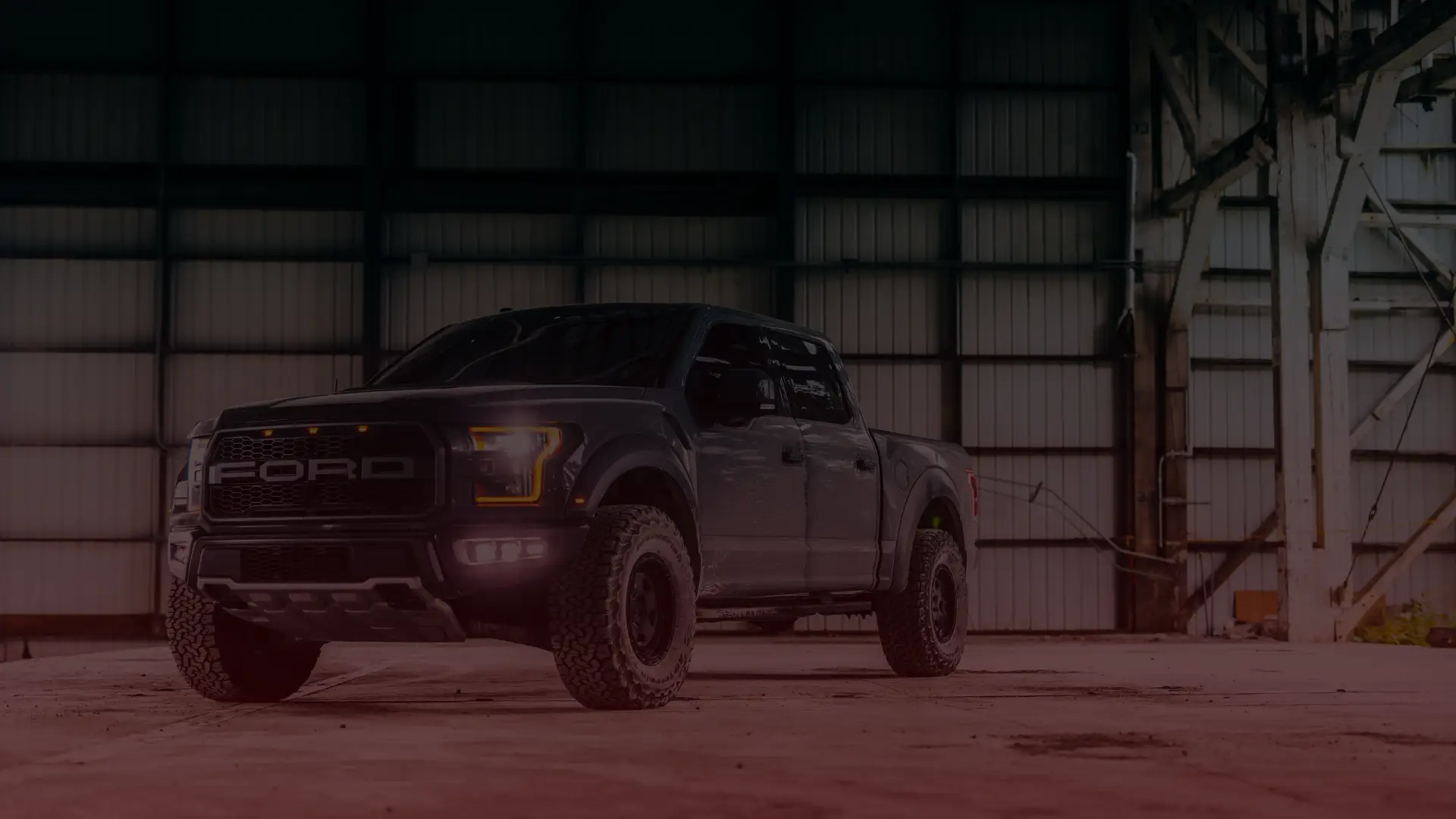 A rugged, black Ford pickup truck is parked inside a spacious, dimly-lit warehouse in Scarborough, with high ceilings and metal beams. The trucks headlights are illuminated, casting light on the dusty concrete floor as if waiting for a skilled Ford mechanic to bring it to life. EuroMechanic | Redline Automotive | Top Reviewed Auto Repair Shop in Scarborough | Visit redlineautomotive.ca