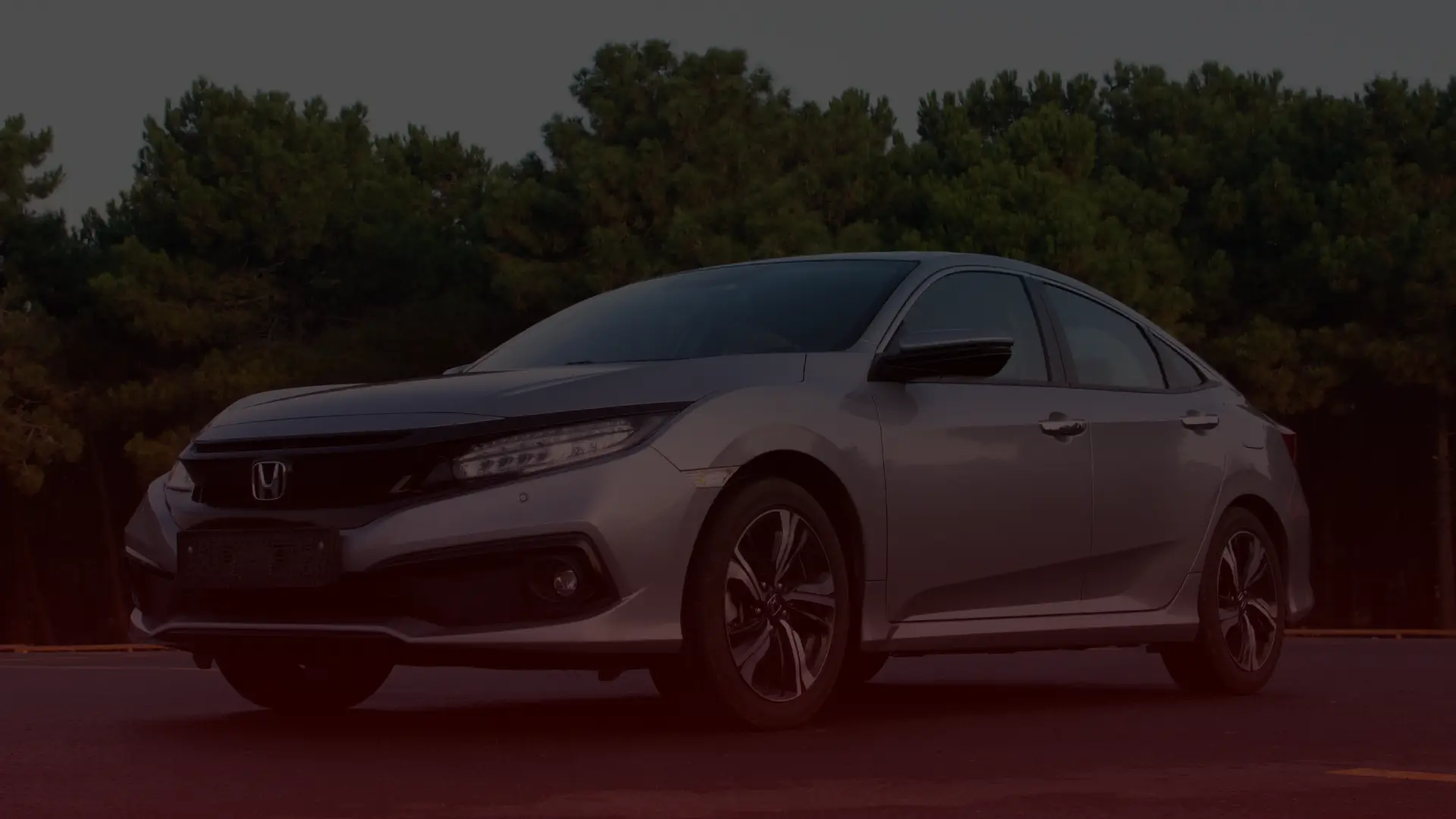 A silver Honda sedan, reminiscent of those expertly maintained by a trusted Honda mechanic in Scarborough, is parked on a deserted road with dense green trees in the background. The car faces left, showcasing its sleek design and modern features against an overcast skys soft shadows. EuroMechanic | Redline Automotive | Top Reviewed Auto Repair Shop in Scarborough | Visit redlineautomotive.ca
