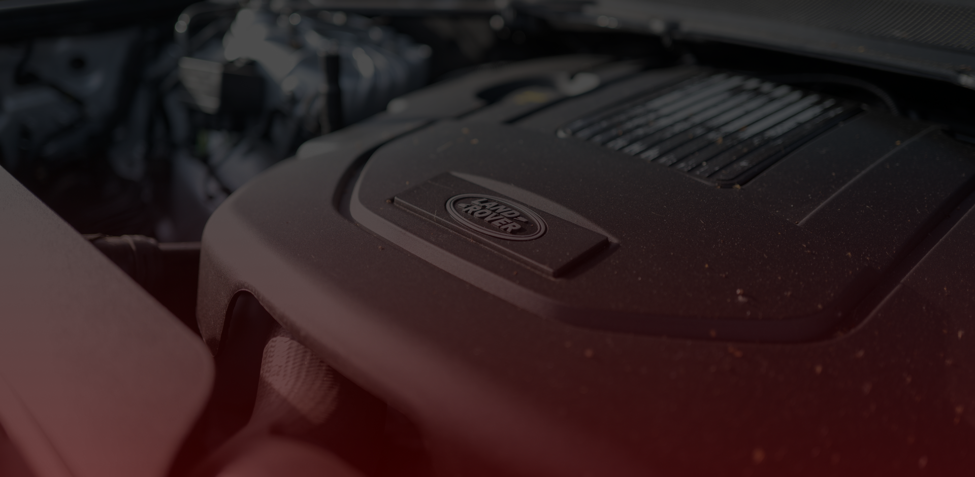 Close-up of an engine showcasing a Land Rover logo. With mostly dark components and a hint of red lighting highlighting its sleek design, the image captures the attention to detail synonymous with any expert Land Rover mechanic in Scarborough, including visible dust particles on the cover. EuroMechanic | Redline Automotive | Top Reviewed Auto Repair Shop in Scarborough | Visit redlineautomotive.ca