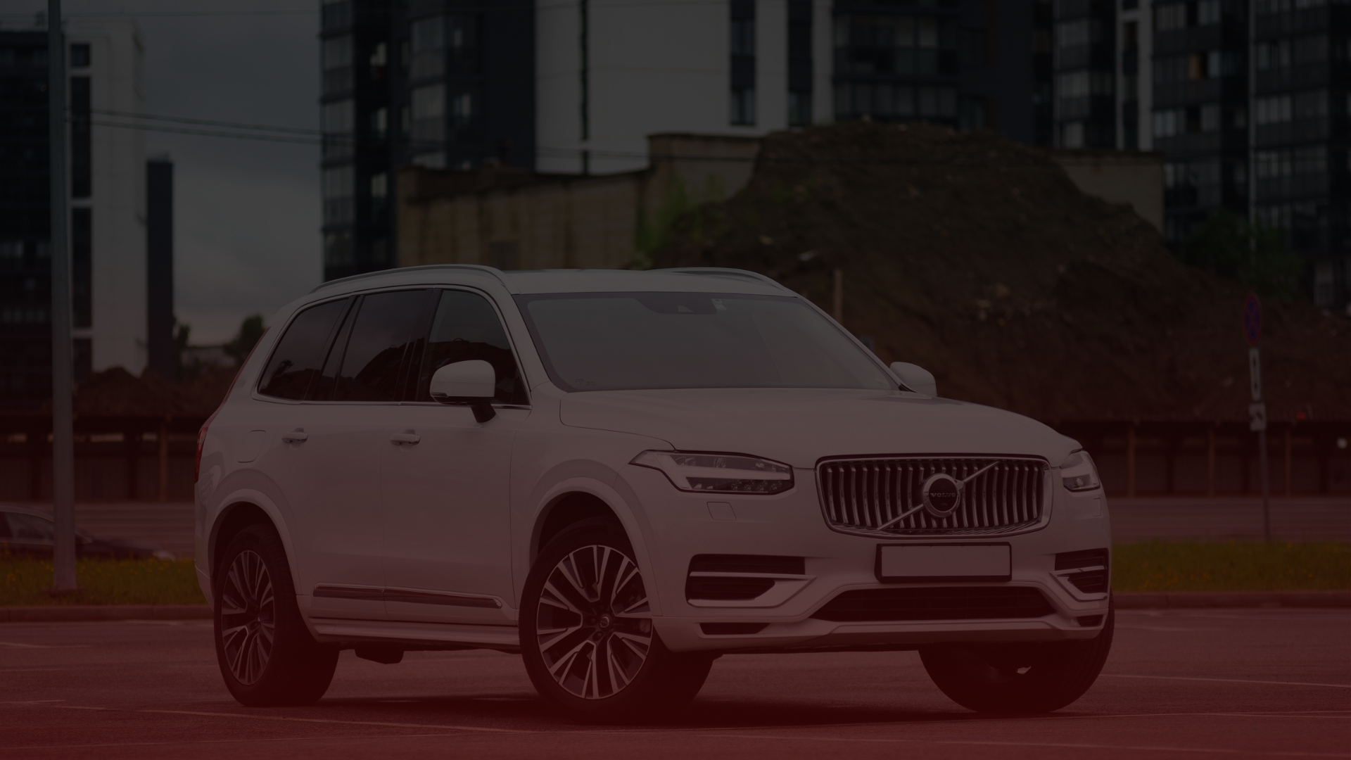 A white Volvo SUV, reminiscent of those often serviced by a trusted Volvo mechanic in Scarborough, is parked in an urban setting with modern buildings in the background. Situated in a parking lot with a mound of earth behind it, the scene exudes a dark, moody atmosphere. EuroMechanic | Redline Automotive | Top Reviewed Auto Repair Shop in Scarborough | Visit redlineautomotive.ca