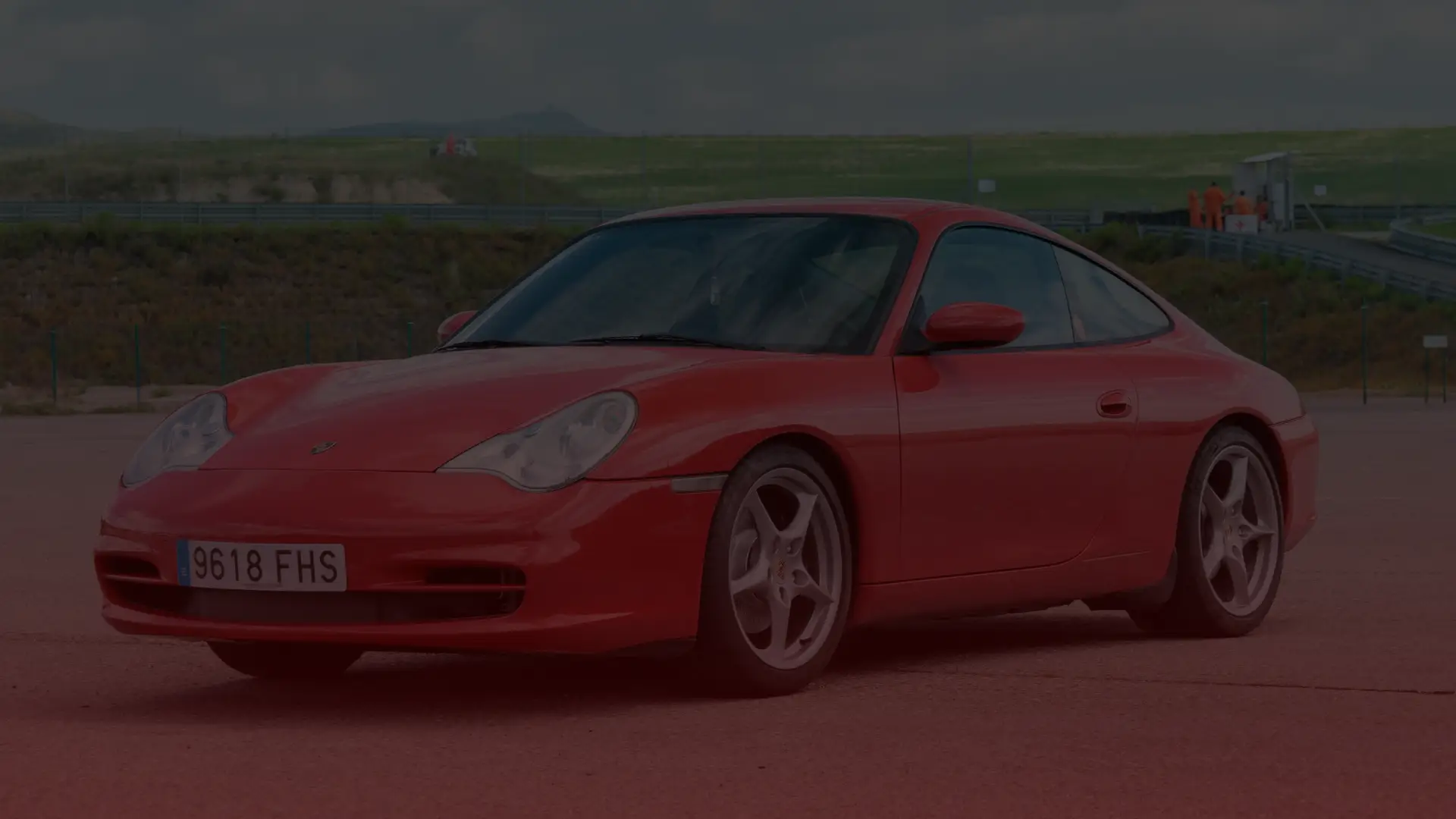 A red sports car, possibly in need of a Porsche repair, is parked on a paved surface against the backdrop of rolling hills and a grassy landscape. Its license plate reads 9618 FHS, under an overcast sky reminiscent of Scarboroughs moody weather. EuroMechanic | Redline Automotive | Top Reviewed Auto Repair Shop in Scarborough | Visit redlineautomotive.ca