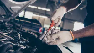 A person wearing gloves is checking a cars oil level using a dipstick. The scene is set in a well-lit automotive garage, with the car hood open and other vehicles in the background. EuroMechanic - Redline Automotive | Top Reviewed Auto Repair Shop in Scarborough | Visit EuroMechanic - Redline Automotive