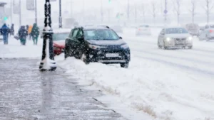 Cars drive down a snow-covered street during heavy snowfall. A sidewalk runs along the left, lined with snow piles, and a few people walk bundled up in winter clothes. Visibility is reduced due to the falling snow. EuroMechanic - Redline Automotive | Top Reviewed Auto Repair Shop in Scarborough | Visit EuroMechanic - Redline Automotive